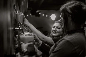 Black and white photo of two women pouring beer at Candid Brewing Company. 