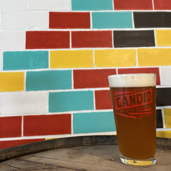A Candid branded pint glass filled with Humdinger beer and in front of a brock wall painted red, blue, brown and yellow.