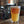 A Candid branded pint glass with a hazy beer in it. In the background, brewing equipment is shown. 