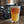 Load image into Gallery viewer, A Candid branded pint glass with a hazy beer in it. In the background, brewing equipment is shown. 
