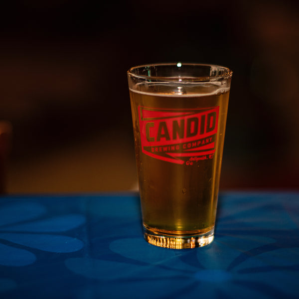 A Candid branded pint glass with beer in it. 
